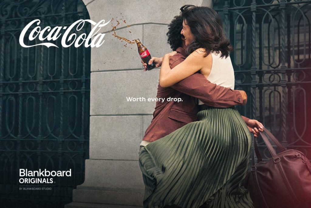 Quảng cáo Coca-Cola in hình hai người đang ôm nhau vui vẻ trên đường phố, với một chai Coca-Cola đang bắn tung tóe nước giải khát. Các văn bản trên hình ảnh bao gồm 'Coca-Cola', 'Worth every drop.', và 'Blankboard ORIGINALS BY BLANKBOARD STUDIO