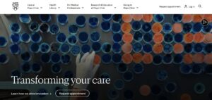A screenshot of the Mayo Clinic website homepage featuring the headline "Transforming your care" over a background image of a gloved hand working with blue and orange petri dishes, with a top navigation menu and a "Request appointment" button.
