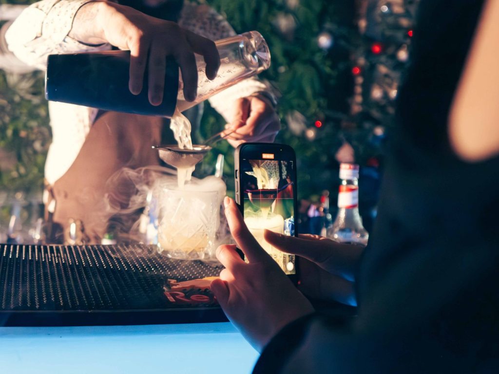 Bartender recording vertical video of a signature cocktail on a smartphone